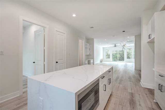 kitchen with light hardwood / wood-style floors, stainless steel microwave, pendant lighting, and a kitchen island