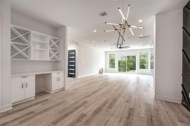 unfurnished living room featuring ceiling fan with notable chandelier and light hardwood / wood-style flooring