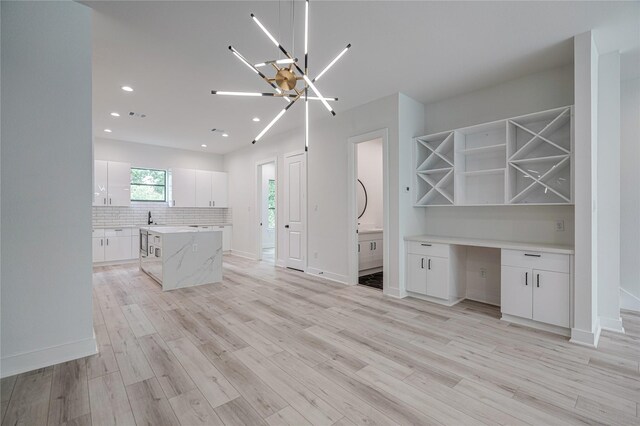 kitchen with white cabinetry, backsplash, light wood-type flooring, and a chandelier