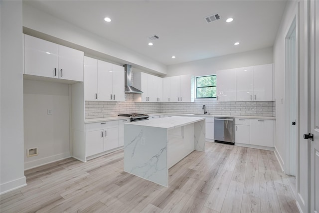 kitchen with white cabinetry, wall chimney range hood, backsplash, light stone countertops, and appliances with stainless steel finishes