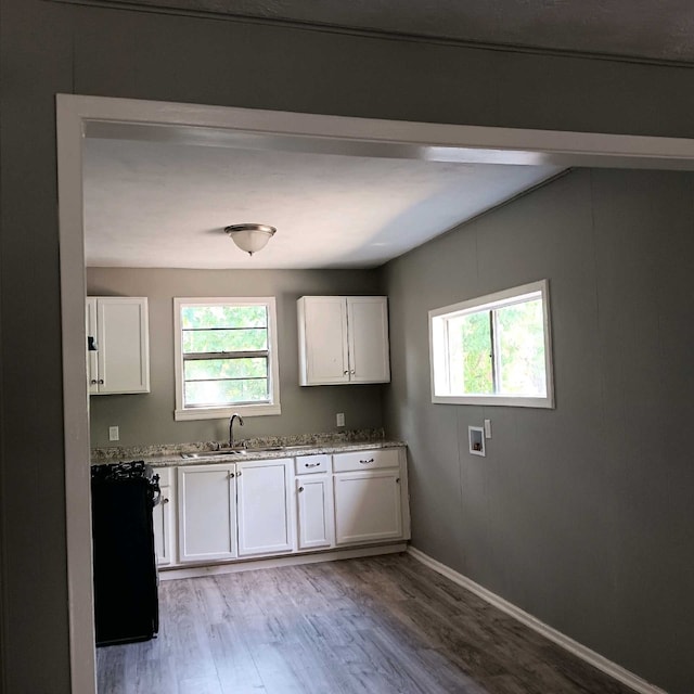 kitchen with sink, light stone counters, white cabinets, and light wood-type flooring