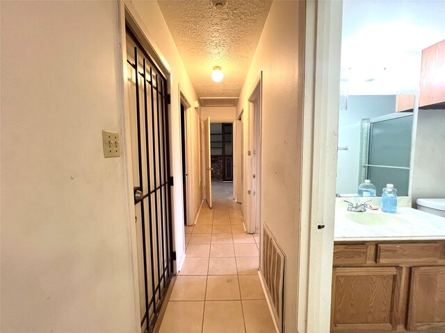 corridor with light tile patterned flooring, sink, and a textured ceiling