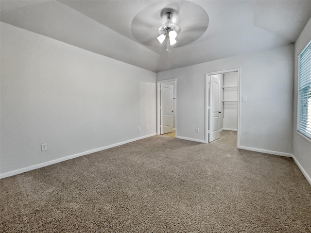 unfurnished bedroom with a walk in closet, a closet, ceiling fan, and carpet flooring