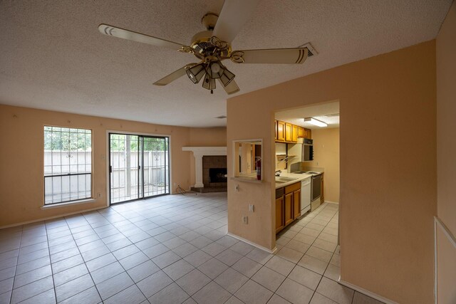 kitchen with a textured ceiling, a tile fireplace, light tile patterned floors, and ceiling fan