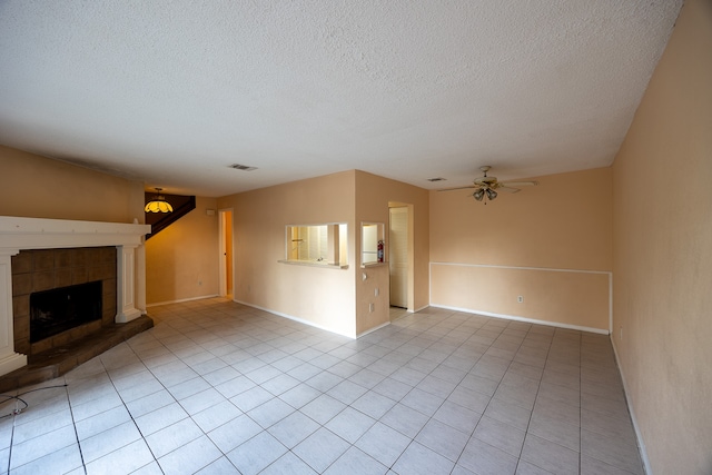 unfurnished living room with a textured ceiling, light tile patterned flooring, a tiled fireplace, and ceiling fan