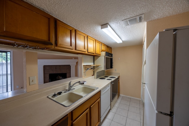 kitchen featuring white appliances, sink, a tile fireplace, a textured ceiling, and light tile patterned flooring