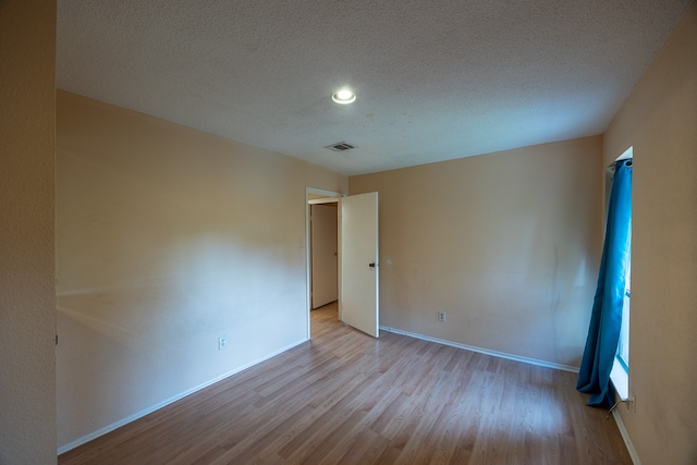 spare room with a textured ceiling and light hardwood / wood-style floors