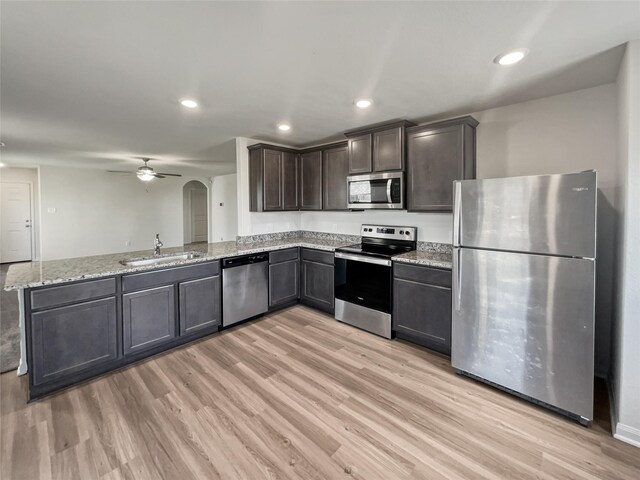 kitchen with appliances with stainless steel finishes, sink, kitchen peninsula, light wood-type flooring, and ceiling fan