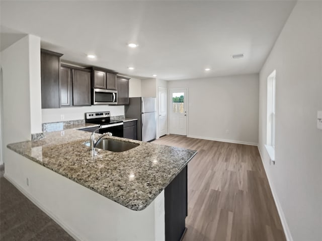 kitchen featuring dark brown cabinets, stainless steel appliances, sink, light stone countertops, and light hardwood / wood-style flooring