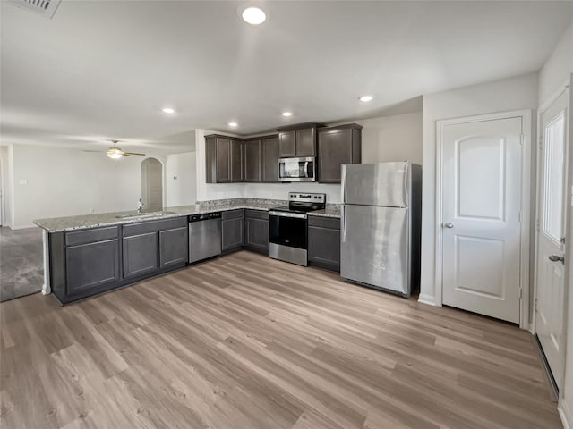 kitchen with dark brown cabinets, light wood-type flooring, stainless steel appliances, light stone countertops, and sink