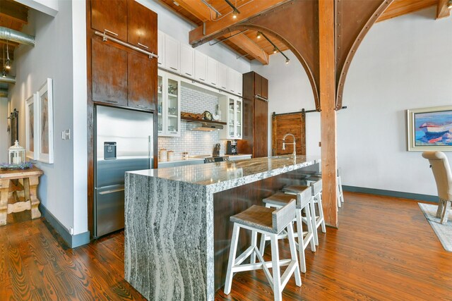 kitchen with white cabinetry, a barn door, tasteful backsplash, stainless steel built in refrigerator, and dark hardwood / wood-style floors