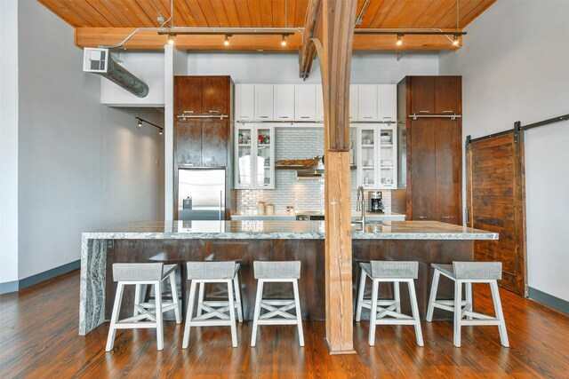 kitchen featuring stainless steel built in refrigerator, a barn door, a kitchen island, white cabinetry, and a kitchen bar