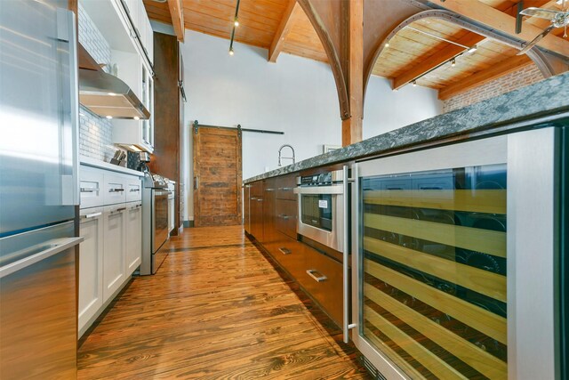 kitchen with beverage cooler, white cabinetry, stainless steel appliances, a barn door, and wood ceiling