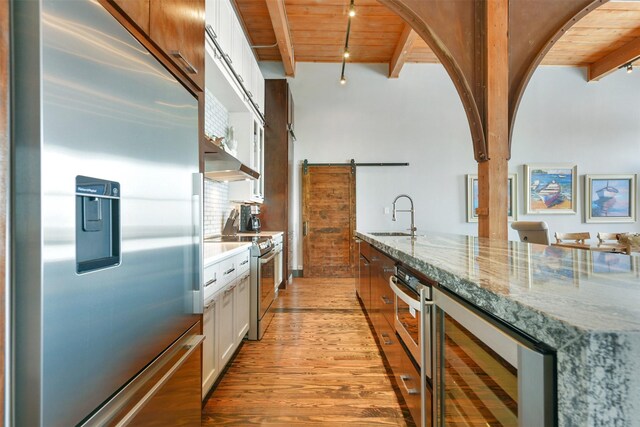 kitchen featuring stainless steel appliances, light stone countertops, white cabinets, a barn door, and wine cooler