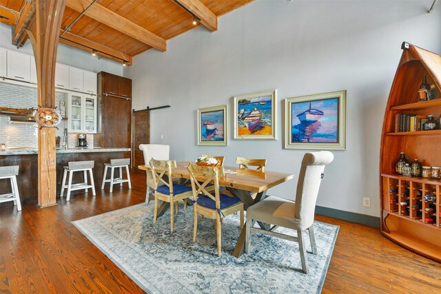 dining area featuring wood ceiling, beamed ceiling, a barn door, and dark hardwood / wood-style flooring