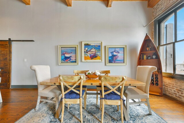 dining area featuring hardwood / wood-style flooring, beamed ceiling, and a barn door