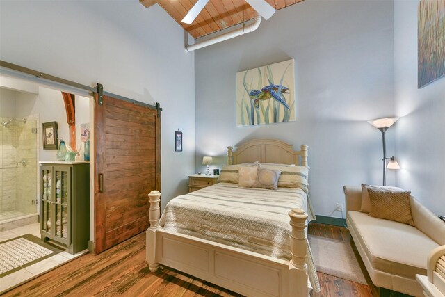 bedroom with hardwood / wood-style flooring, a towering ceiling, a skylight, and a barn door