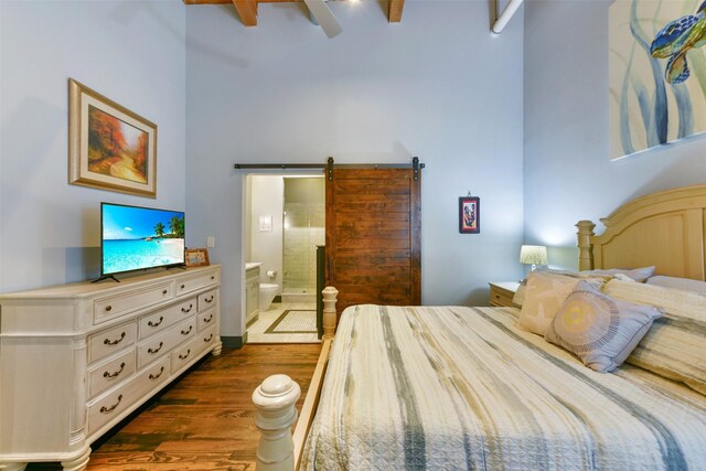 bedroom featuring a towering ceiling, connected bathroom, ceiling fan, dark hardwood / wood-style flooring, and a barn door