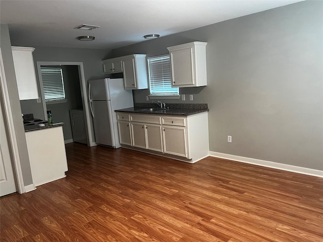 kitchen featuring dark wood-style flooring, visible vents, freestanding refrigerator, a sink, and baseboards