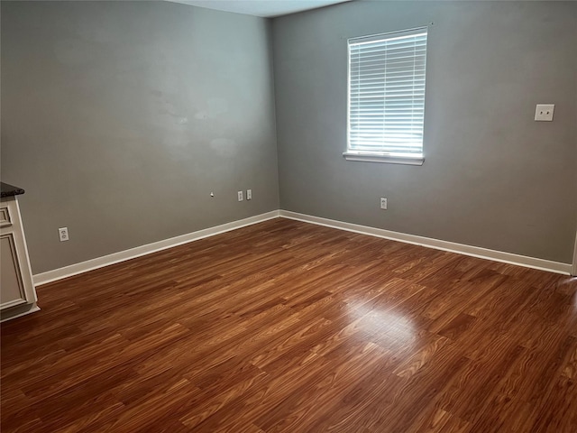 spare room with baseboards and dark wood-type flooring