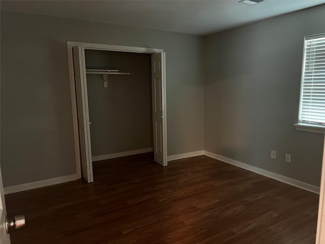 unfurnished bedroom featuring a closet, dark wood finished floors, and baseboards