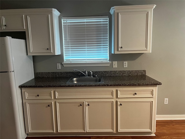 kitchen featuring baseboards, dark stone countertops, wood finished floors, freestanding refrigerator, and a sink