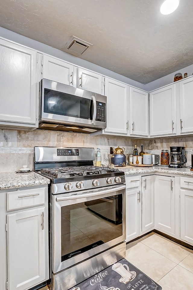 kitchen featuring appliances with stainless steel finishes, tasteful backsplash, light tile patterned floors, light stone countertops, and white cabinetry