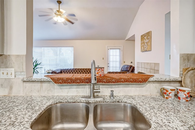 kitchen featuring vaulted ceiling, light stone counters, sink, and ceiling fan