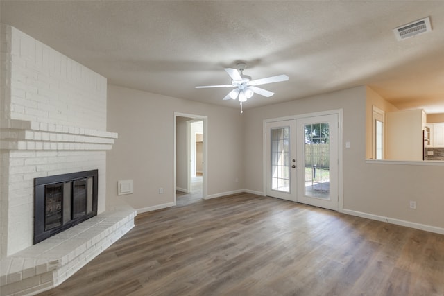 unfurnished living room featuring a textured ceiling, ceiling fan, brick wall, a fireplace, and wood-type flooring