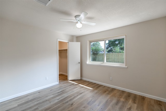 unfurnished bedroom with a spacious closet, a closet, a textured ceiling, ceiling fan, and wood-type flooring