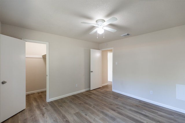 unfurnished bedroom with a spacious closet, ceiling fan, hardwood / wood-style floors, and a closet