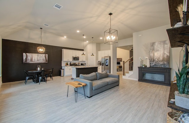 living room featuring light wood finished floors, visible vents, stairway, a fireplace, and high vaulted ceiling