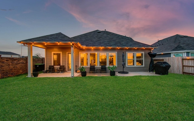 back of house featuring a shingled roof, fence, a patio, and a lawn