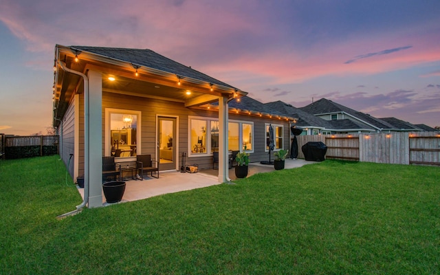 back of property at dusk with a patio area, a fenced backyard, and a lawn