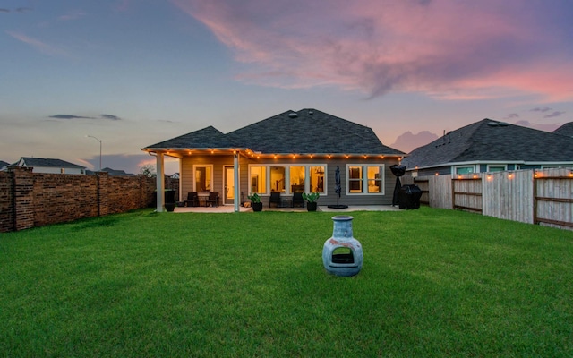 back of house at dusk featuring a fenced backyard, a patio, and a yard