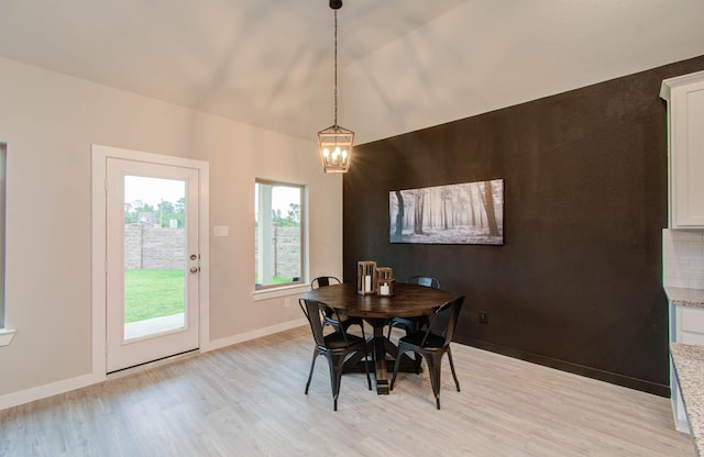 dining area featuring a chandelier, baseboards, vaulted ceiling, and light wood finished floors