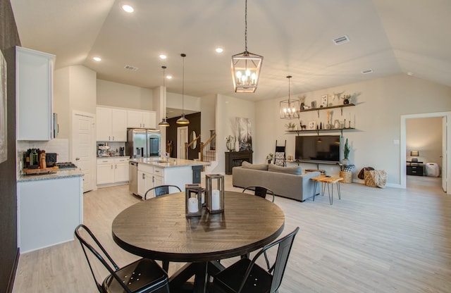 dining space featuring light wood finished floors, stairway, visible vents, and vaulted ceiling