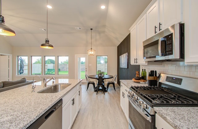 kitchen featuring vaulted ceiling, stainless steel appliances, a sink, and white cabinetry