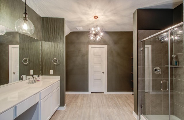 bathroom featuring an inviting chandelier, a stall shower, vanity, wood finished floors, and baseboards