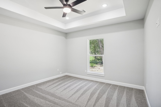 carpeted spare room featuring a tray ceiling and ceiling fan