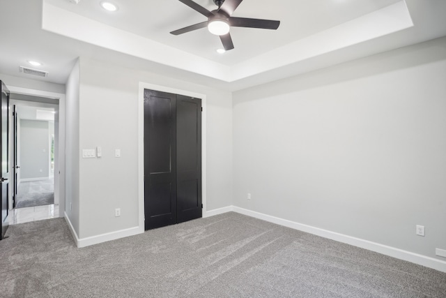 unfurnished bedroom featuring ceiling fan, carpet floors, a closet, and a raised ceiling