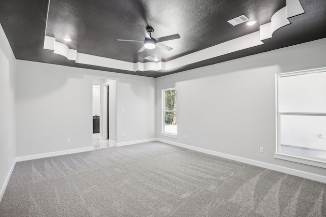 carpeted empty room featuring a tray ceiling, ceiling fan, and a textured ceiling