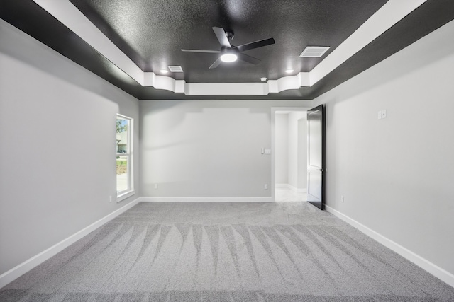 carpeted empty room with ceiling fan, a textured ceiling, and a tray ceiling