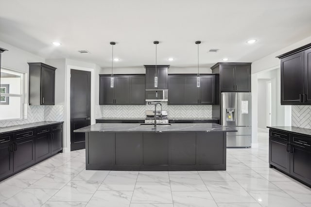 kitchen featuring appliances with stainless steel finishes, dark stone countertops, a kitchen island with sink, and decorative light fixtures