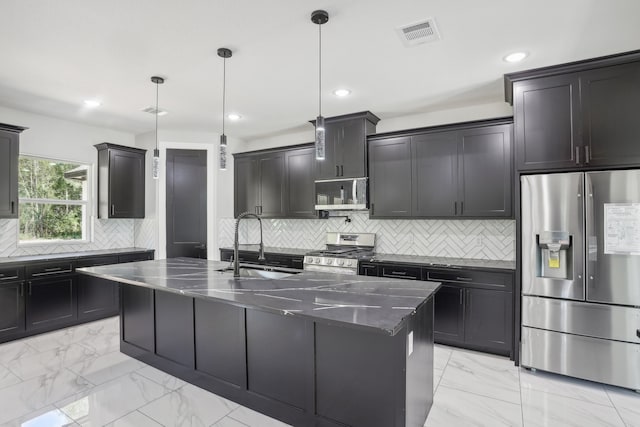 kitchen with backsplash, a center island with sink, appliances with stainless steel finishes, and hanging light fixtures