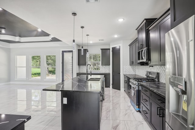 kitchen with an island with sink, hanging light fixtures, sink, stainless steel appliances, and decorative backsplash