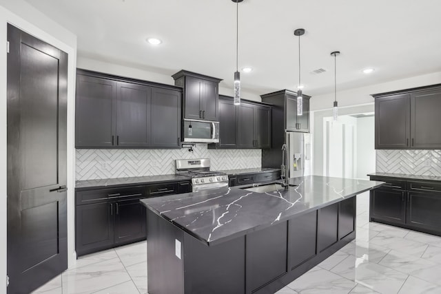 kitchen with stainless steel appliances, backsplash, a center island with sink, and hanging light fixtures