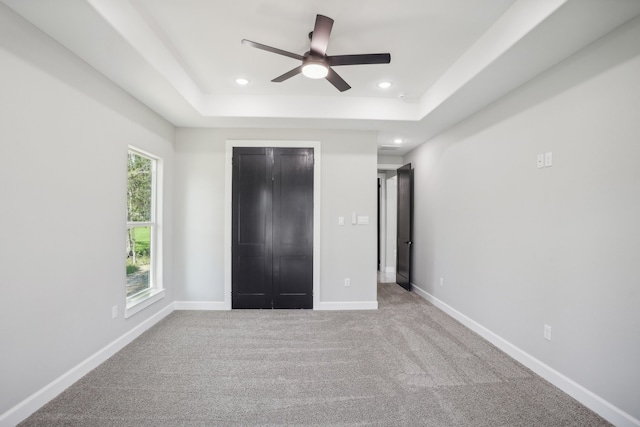 unfurnished bedroom featuring a tray ceiling, multiple windows, and ceiling fan