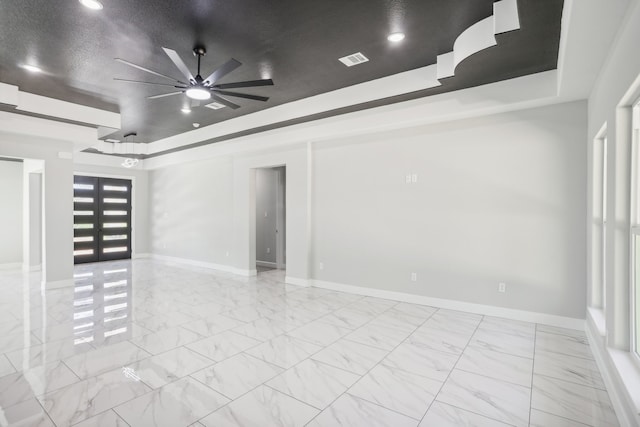 empty room with a tray ceiling, ceiling fan, and a textured ceiling