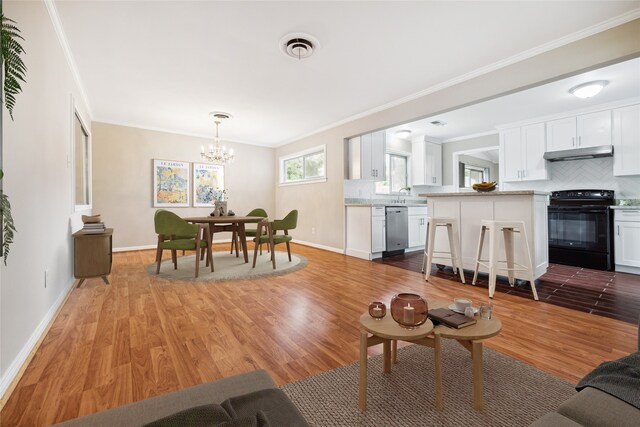 living room with a notable chandelier, sink, ornamental molding, and hardwood / wood-style flooring